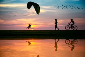 People enjoying outdoor activities at sunset – cycling, running, and paragliding – part of GetYourGuide experiences with Urbe Travel