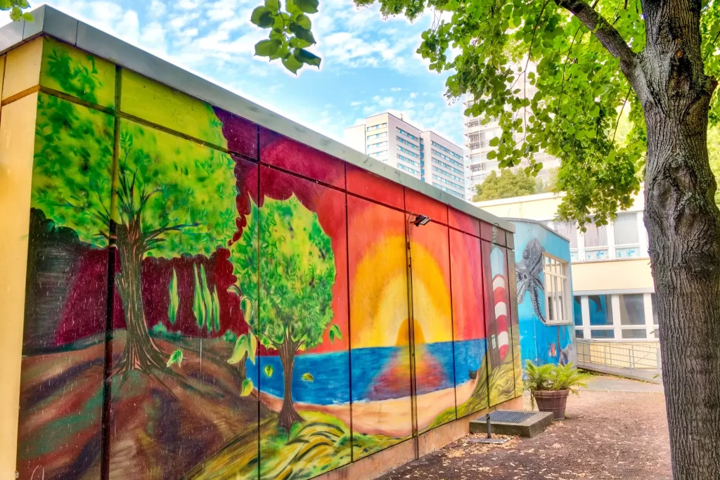 Colorful street art mural in Berlin with forest and sunset landscape.