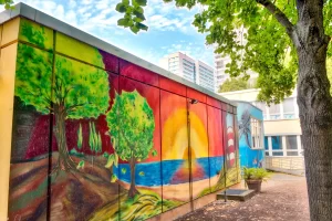 Colorful street art mural in Berlin with forest and sunset landscape.