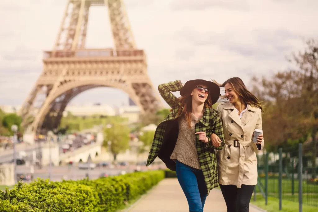 Two young female travelers enjoying coffee near Eiffel Tower in Paris, representing tourist tax benefits in Europe