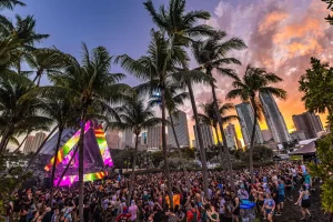 Crowd dancing at Ultra Miami 2026 EDM festival at Bayfront Park with palm trees and Miami skyline at sunset.